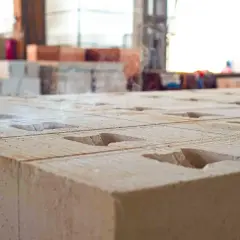 Zbliżenie na betonowe bloczki z otworami. W tle widać palety z materiałami budowlanymi. Ile bloczków betonowych na m2?