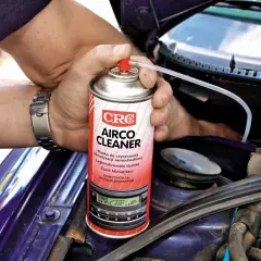 Ręce z zegarkiem trzymają puszkę "Airco Cleaner" do czyszczenia klimatyzacji. Zastanawiasz się, ile kosztuje nabicie klimatyzacji? Ten produkt może pomóc.