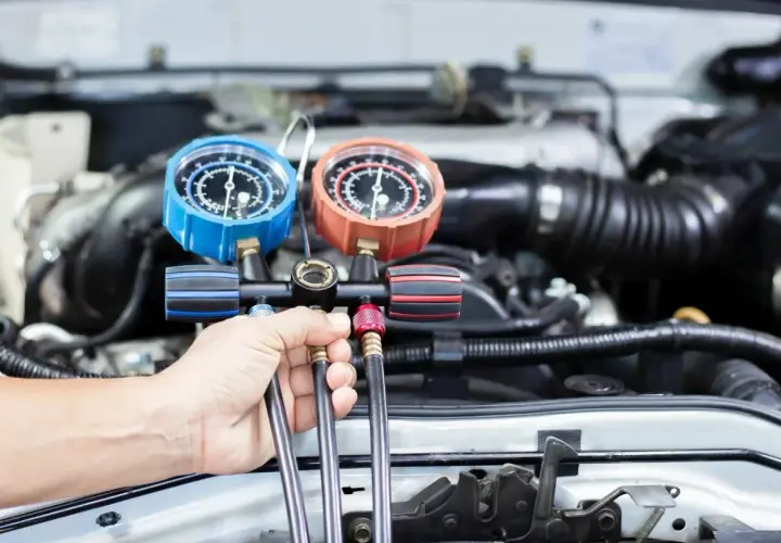 Mechanik sprawdza ciśnienie czynnika r1234yf w układzie klimatyzacji samochodu za pomocą manometrów.