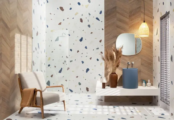 Nowoczesna łazienka z podłogą i ścianami w stylu **terrazzo**, drewnianymi akcentami, fotelem i niebieską umywalką.