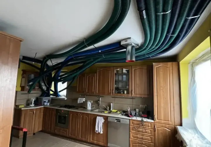 W kuchni starego domu instalacja rekuperacji tworzy gęstą sieć zielonych i niebieskich rur na suficie, przypominając futurystyczny system wentylacyjny.
