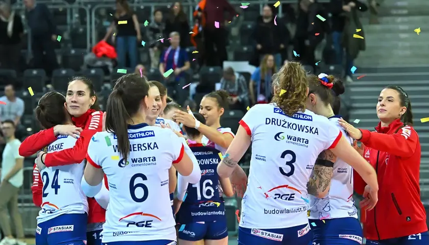 Siatkarki w strojach sportowych przytulają się, obsypane konfetti.