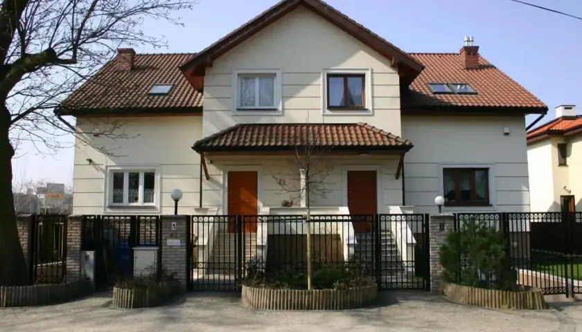 Jasny dom wielorodzinny z dwoma wejściami, ogrodzony czarnym płotem.