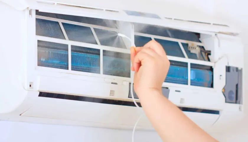 Czyszczenie klimatyzacji w domu. Ręka spryskuje wnętrze urządzenia, dbając o odgrzybianie i świeże powietrze.