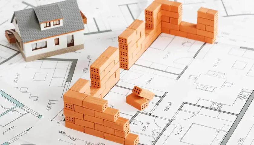 Model domu i mury z cegieł na planie architektonicznym symbolizują początek budowy domu.