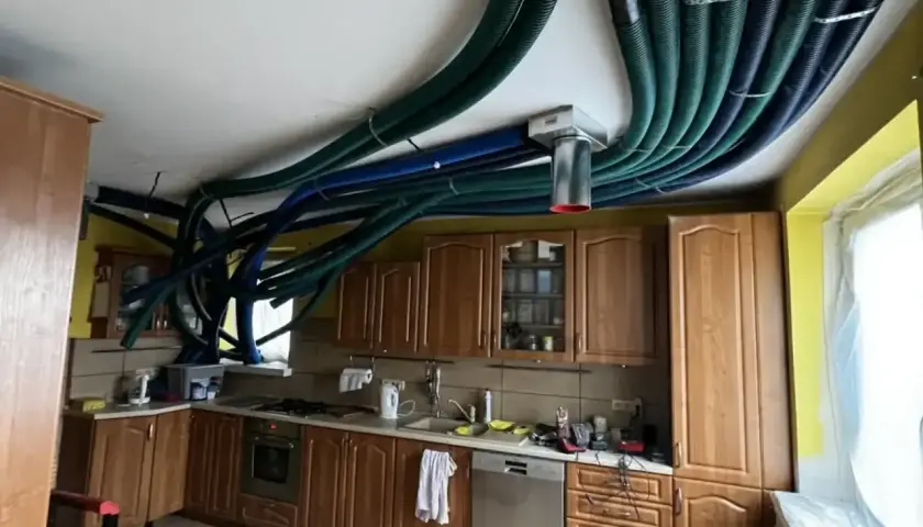 W kuchni starego domu instalacja rekuperacji tworzy gęstą sieć zielonych i niebieskich rur na suficie, przypominając futurystyczny system wentylacyjny.
